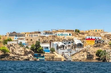 A Nubian village of brightly painted houses on the Nile bank at Aswan, seen from the water.