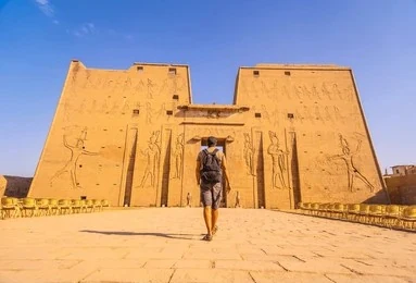 The great pylon of the Temple of Horus at Edfu, a visitor walking towards its gateway.
