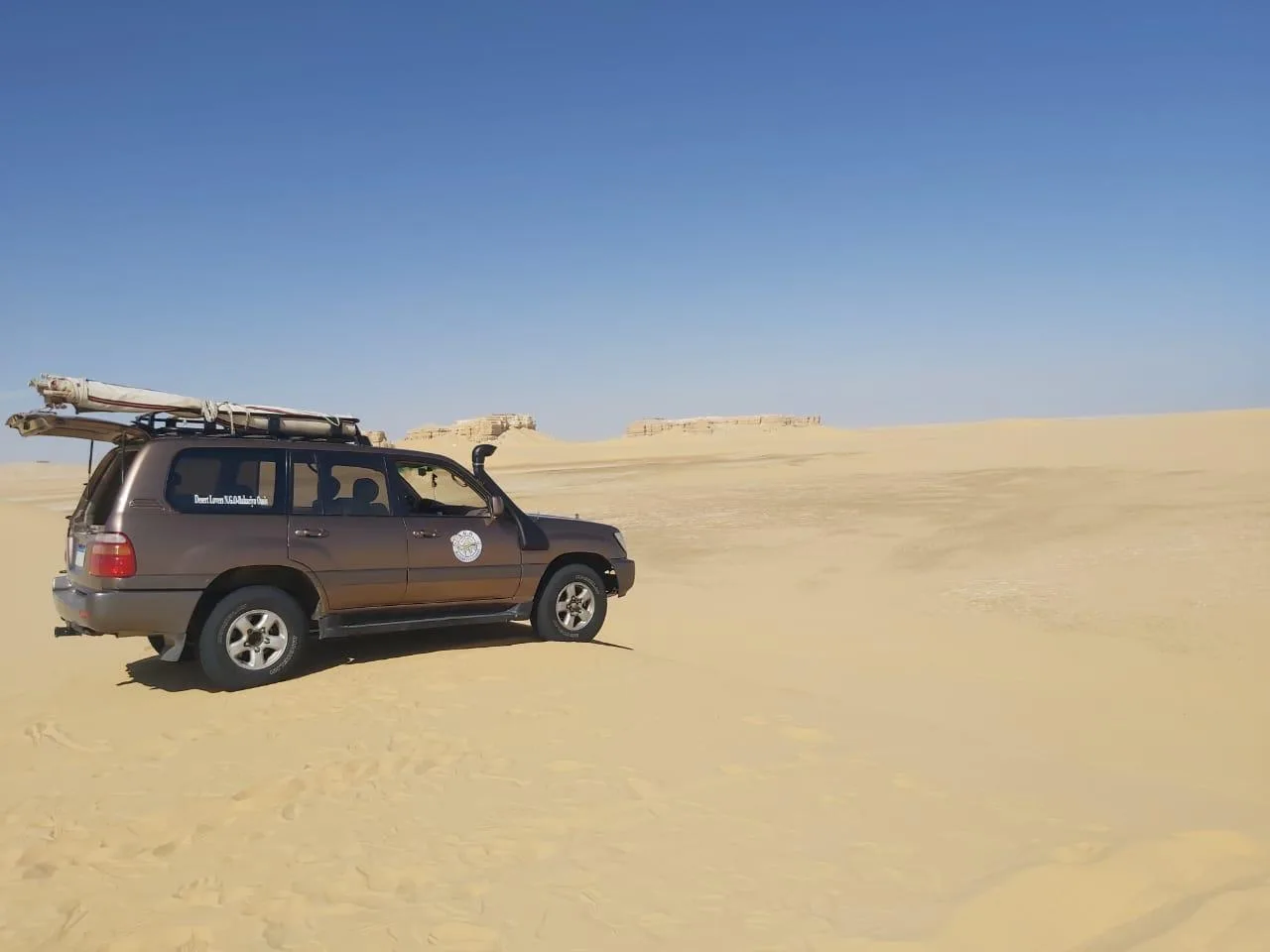 A 4x4 parked on pale sand beneath a deep blue sky in the Fayoum desert