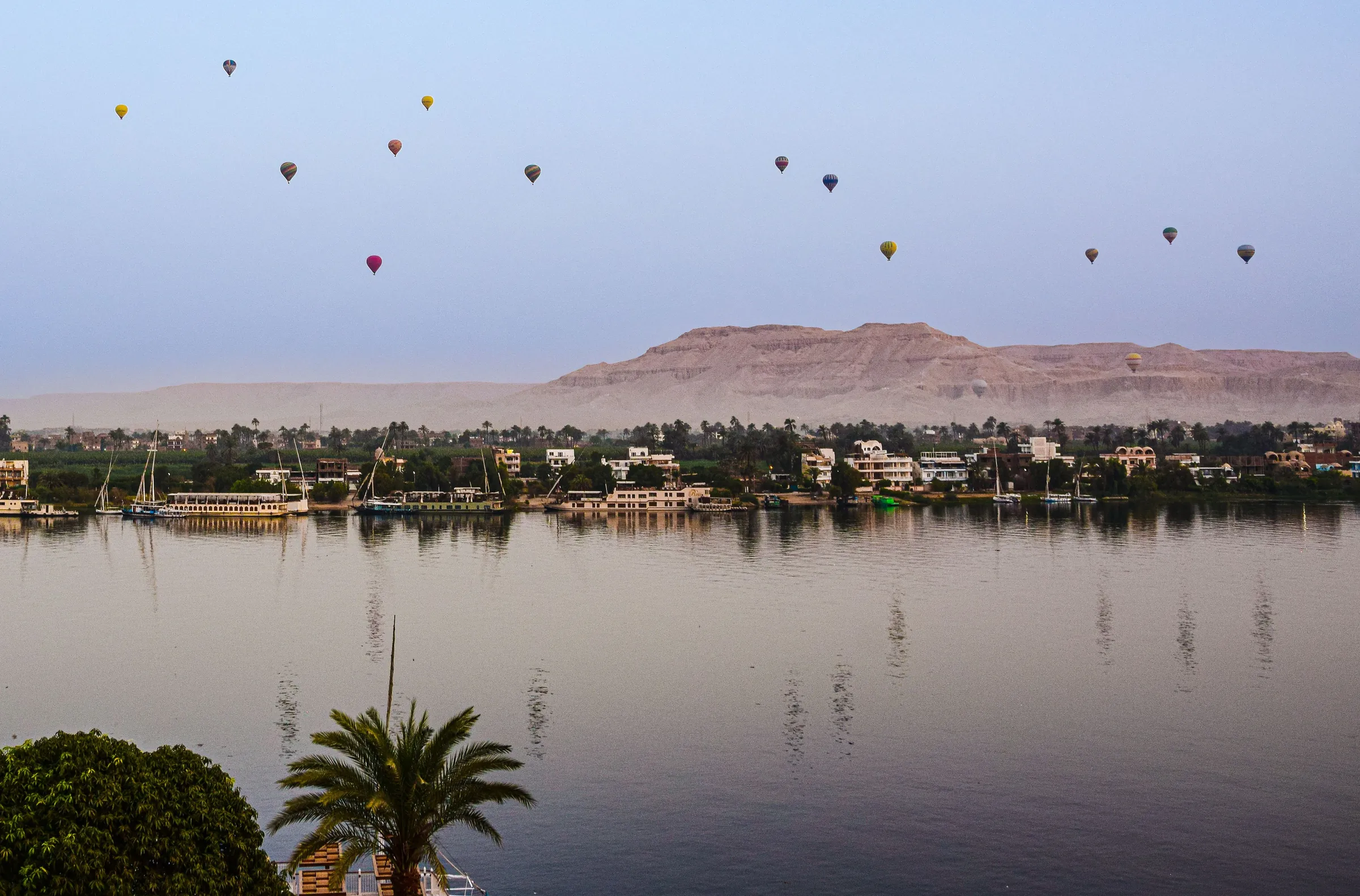 Hot-air balloons over the Nile at Luxor at dawn, the West Bank hills behind.