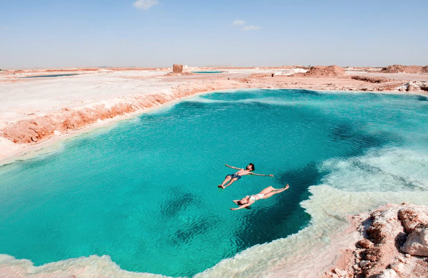 Two swimmers floating in a turquoise salt lake in Siwa
