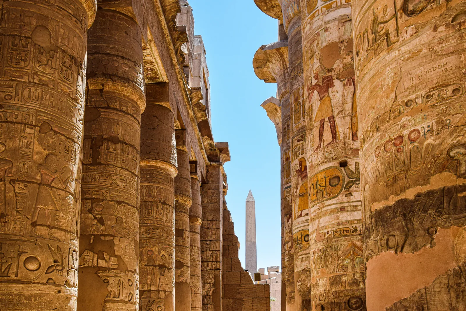 Visit Egypt — carved columns of Karnak Temple with an obelisk beyond